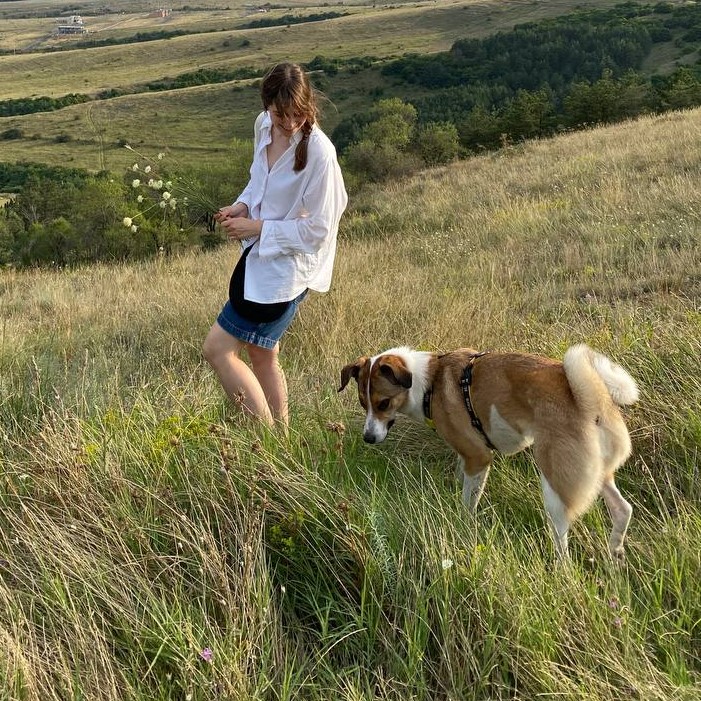 A person standing in a grassy field holding white flowers, with a dog nearby.