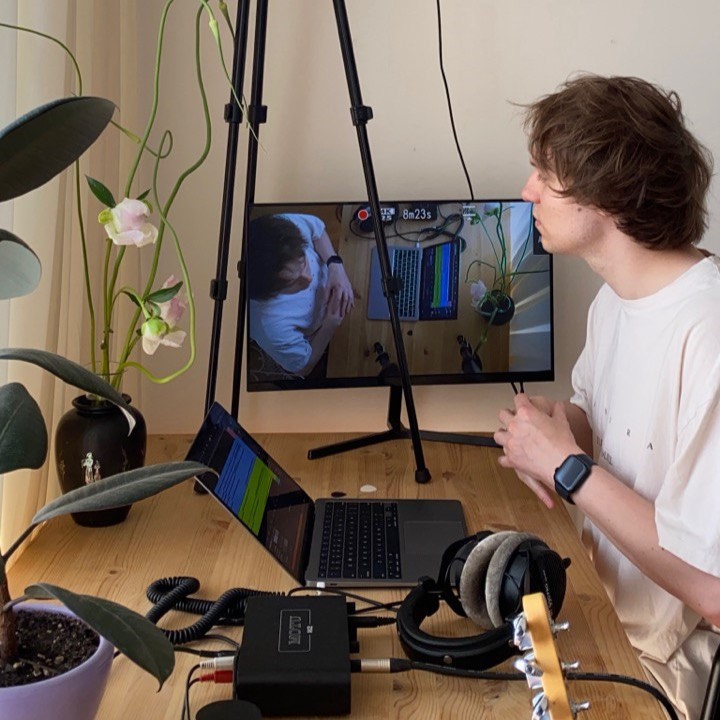 A person sitting at a desk with a computer, headphones, and plants.